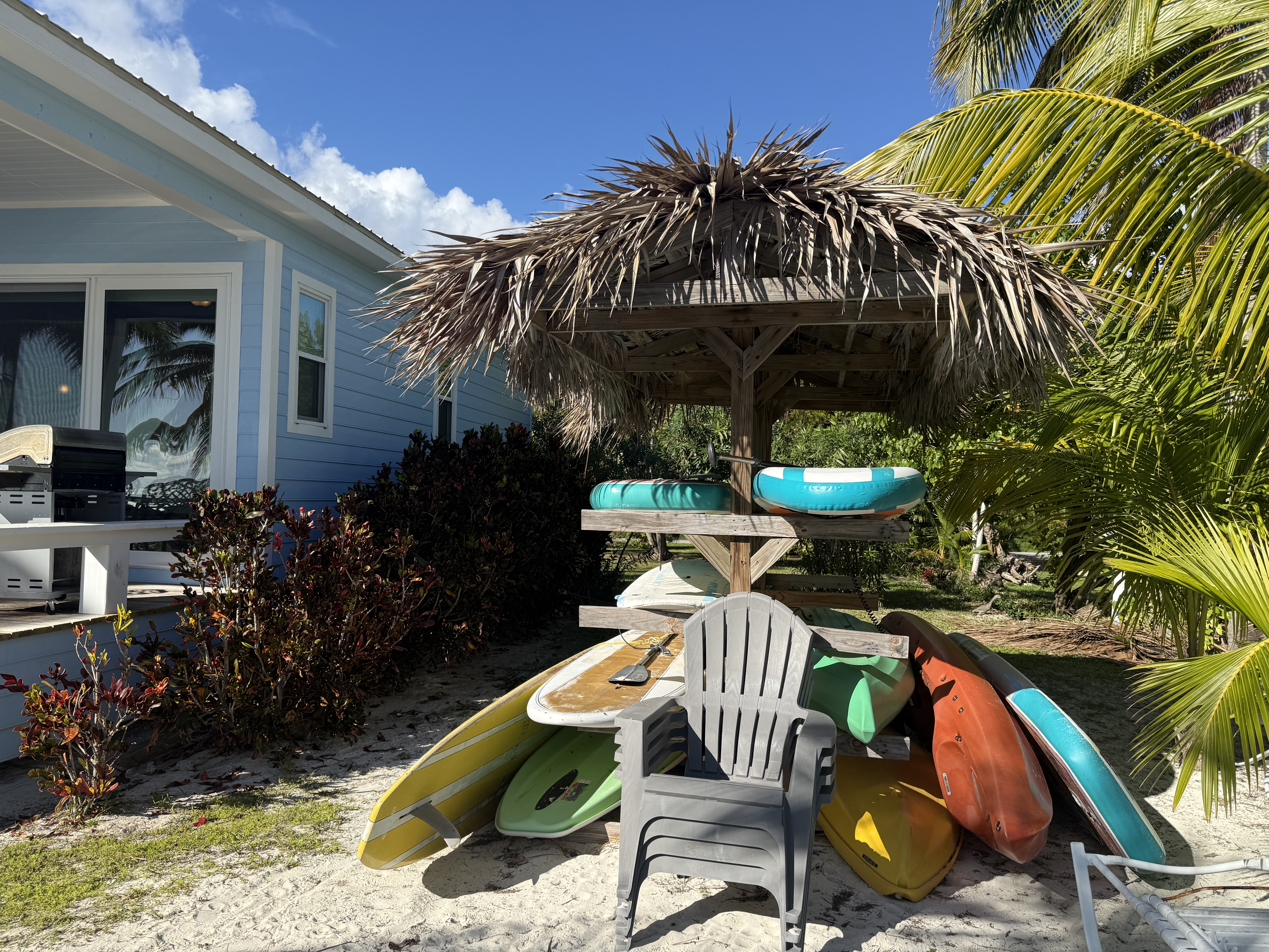 Tiki hut with kayaks and paddle boards, and chairs for sitting on the beach