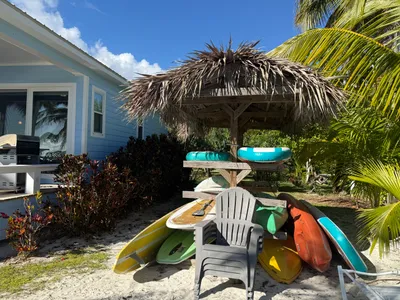 Tiki hut with kayaks and paddle boards, and chairs for sitting on the beach
